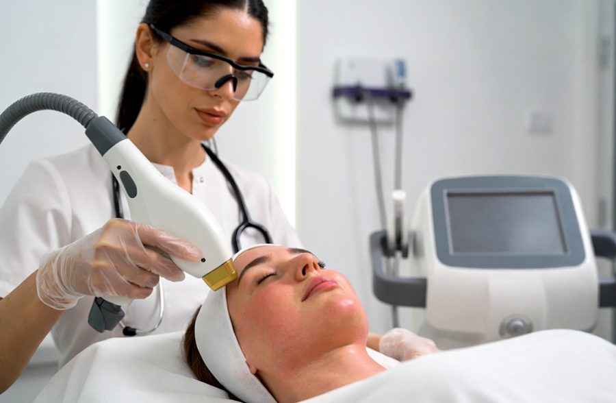 High-resolution professional aesthetic clinic image showing a female client receiving laser hair removal treatment on her face in a modern dermatology clinic in Rawalpindi. The technician is wearing medical gloves and protective eyewear while using an advanced laser hair removal machine. Clean white clinical environment, soft natural lighting, professional skincare setting, minimal and hygienic interior. The client appears relaxed and comfortable. Corporate and medical aesthetic style, realistic photography, suitable for an SEO article about permanent laser hair removal and Deaesthetic Lounge Rawalpindi.